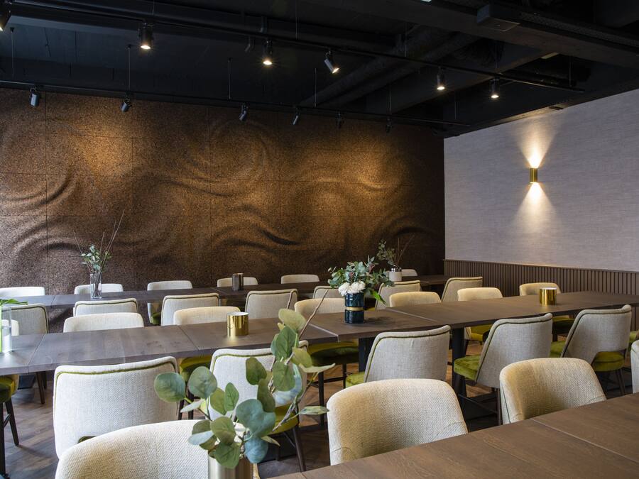 Une salle de conférence dotée de plusieurs tables et chaises, d’un mur à texture et d’un luminaire moderne.