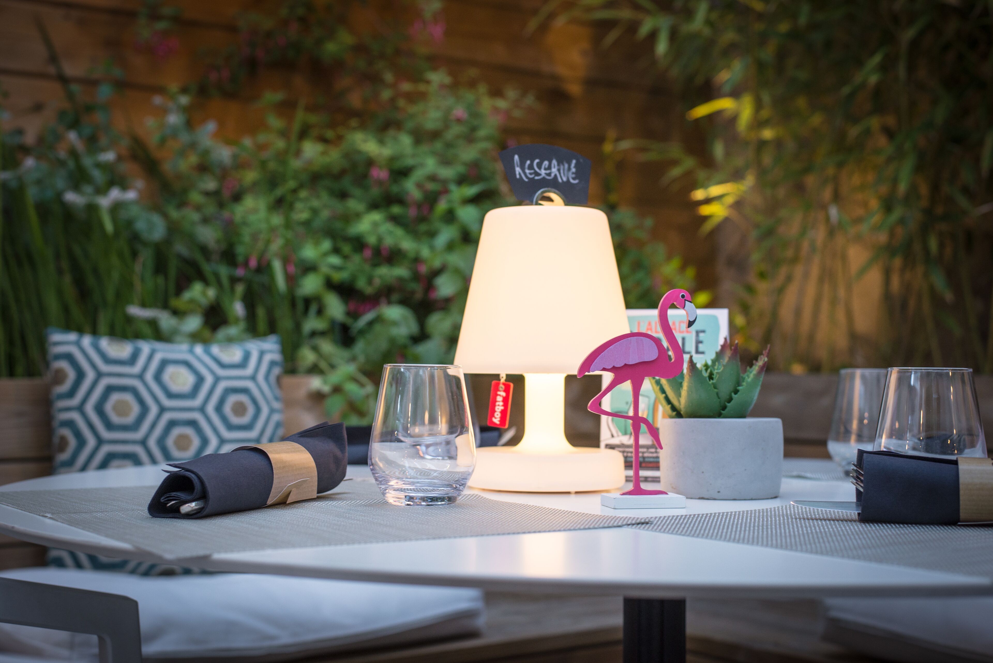 A table set with a lamp, glasses, a napkin, a decorative flamingo, and a sign that says "RESERVE".