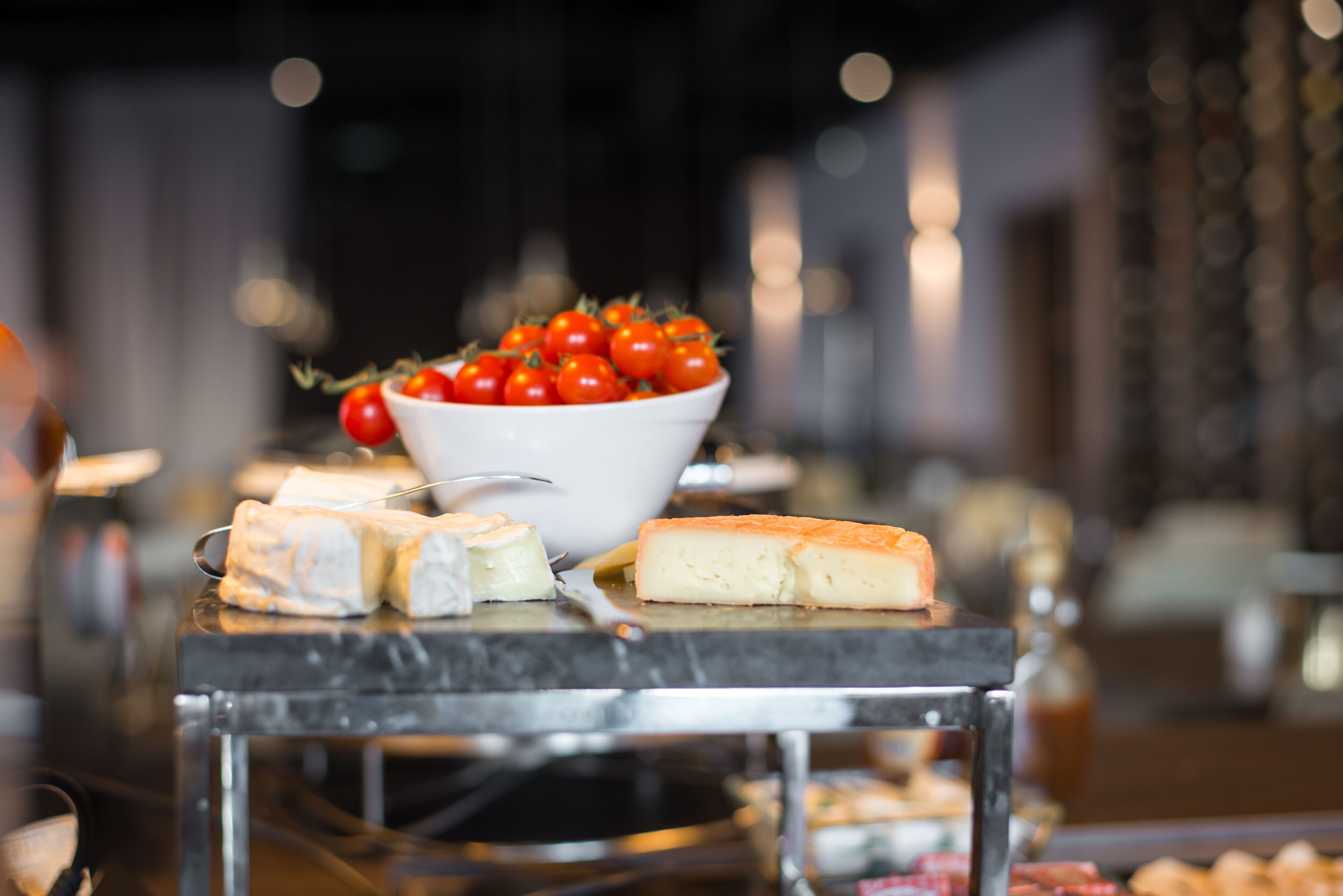 A buffet table with various cheeses and a bowl of cherry tomatoes.