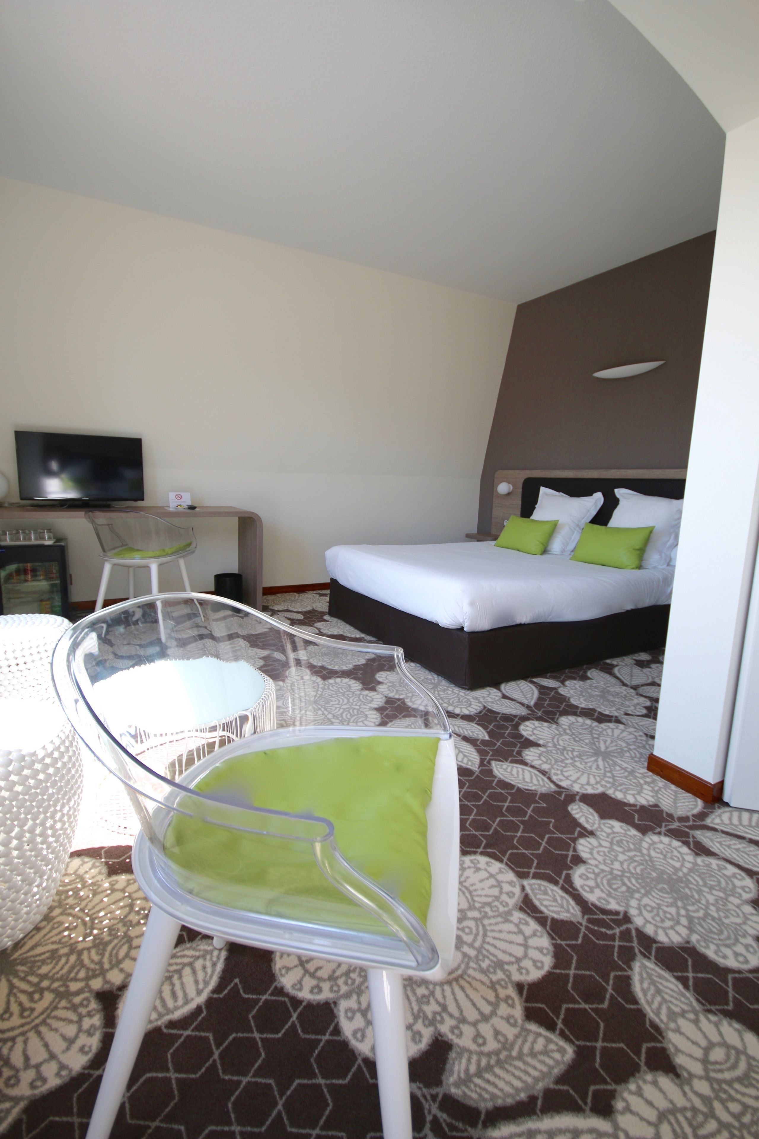 Ein Hotelzimmer mit einem Bett, einem Schreibtisch mit Fernseher, einem Sessel und einem Glastisch.