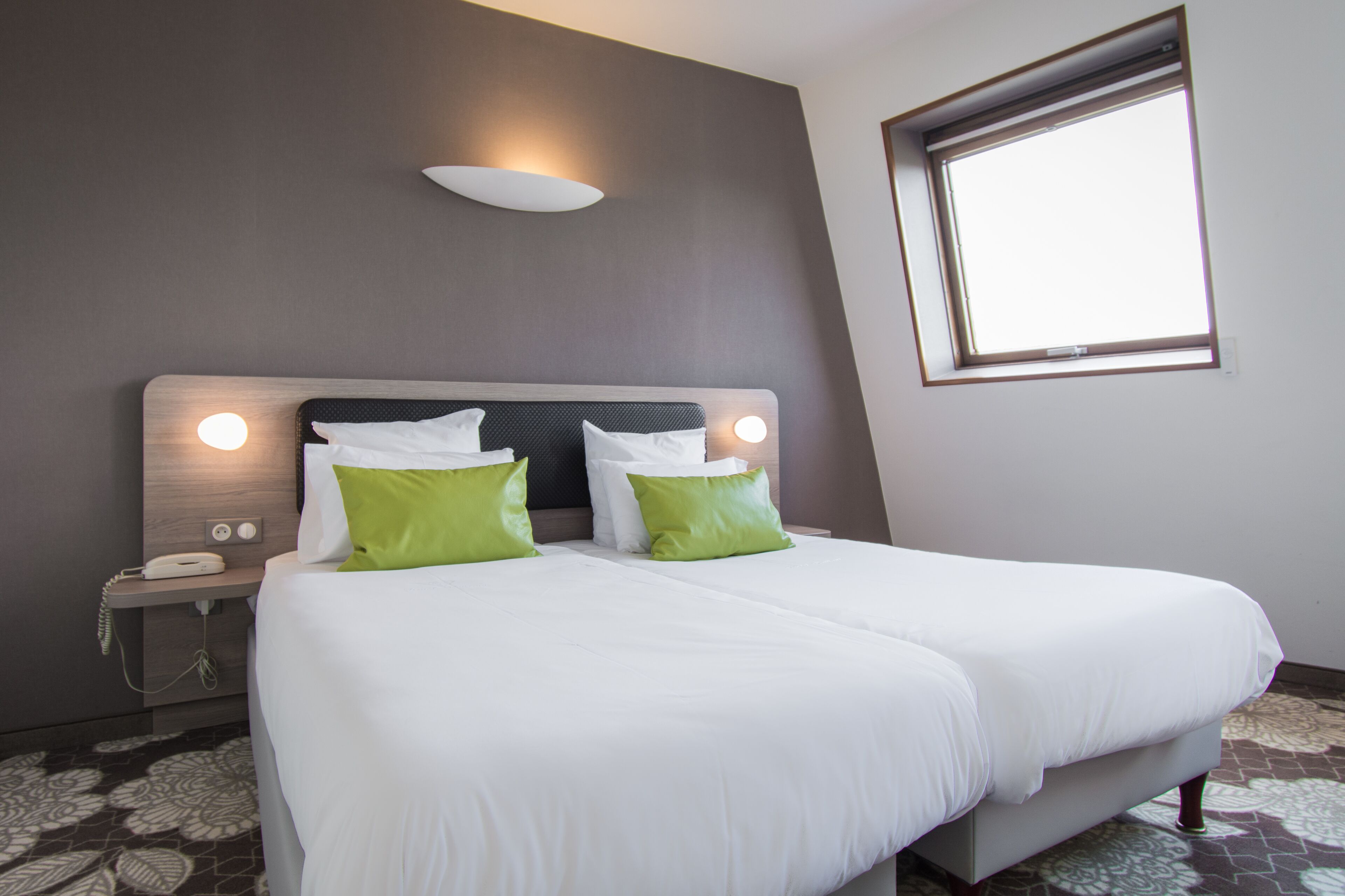 Un lit double avec des oreillers blancs et verts, un téléphone sur la table de chevet et un luminaire fixé au mur.