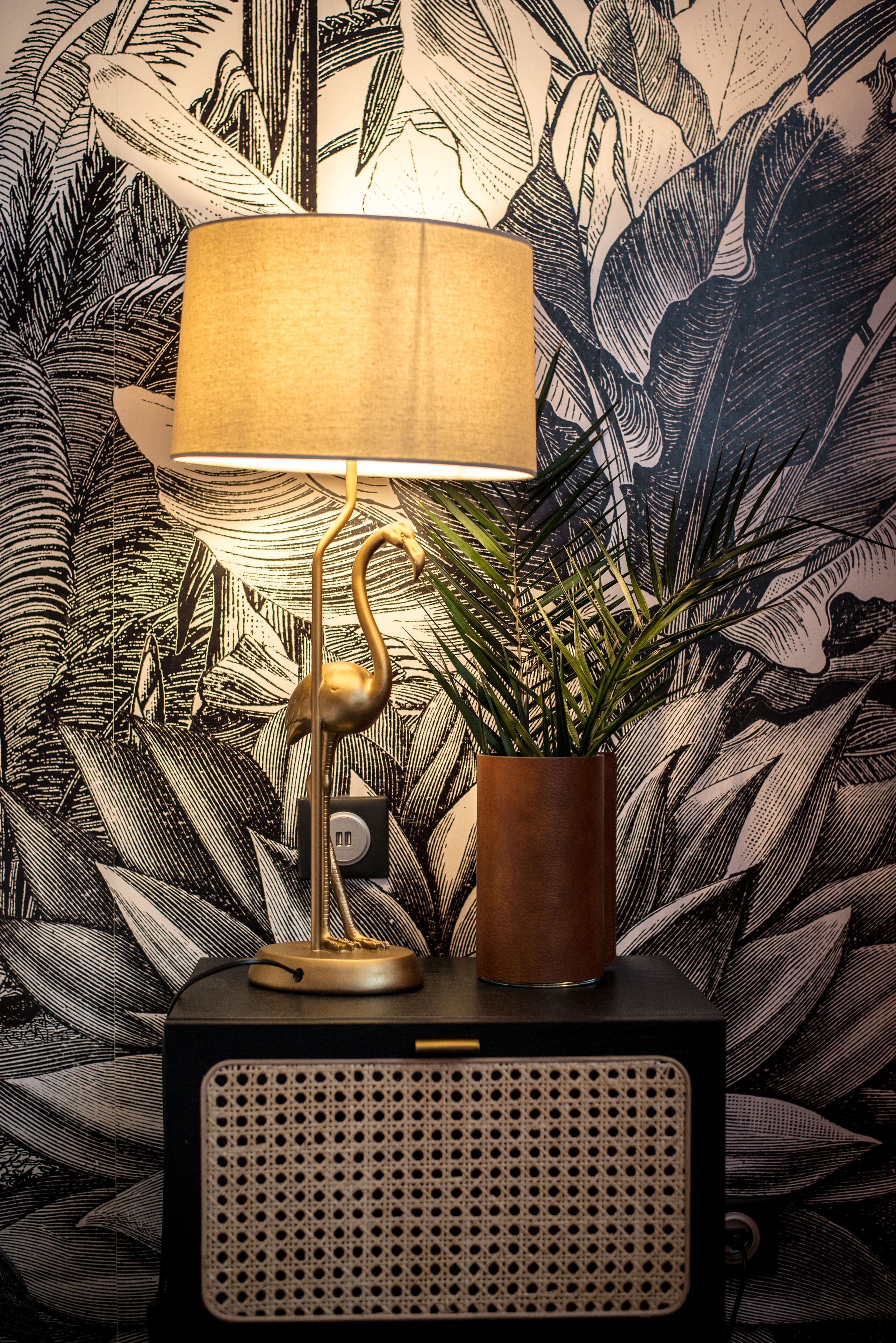Une lampe avec un pied doré et un abat-jour blanc, une plante en pot et une radio ancienne dont la façade est perforée.