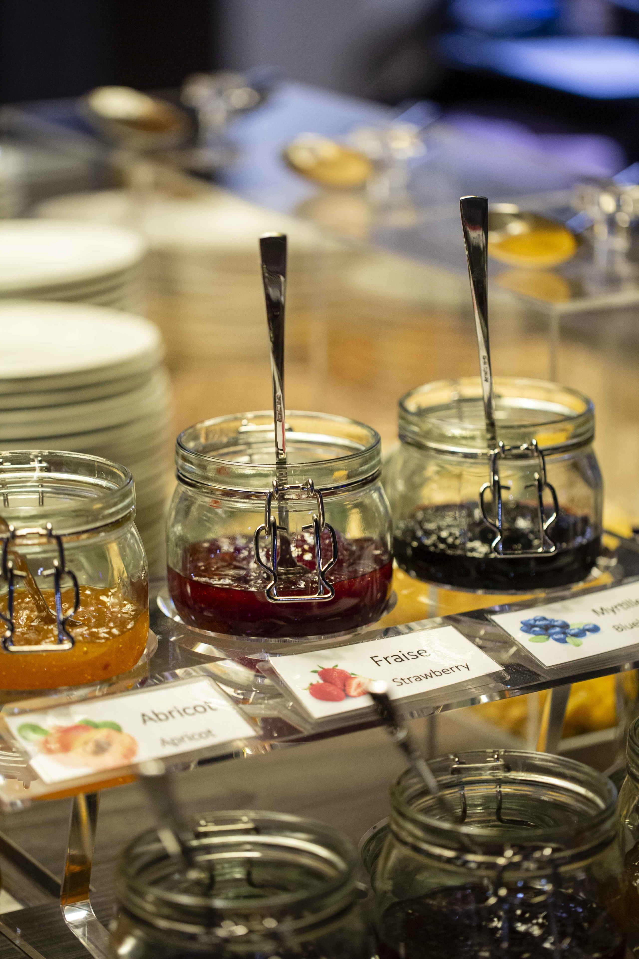 Un buffet proposant une variété de pots de confitures et de conserves, notamment à l’abricot et à la fraise.