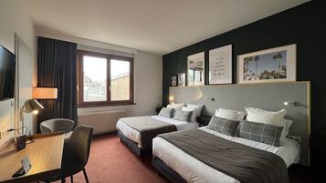 A hotel room with two beds, a desk, a chair, a TV, and a window with curtains.