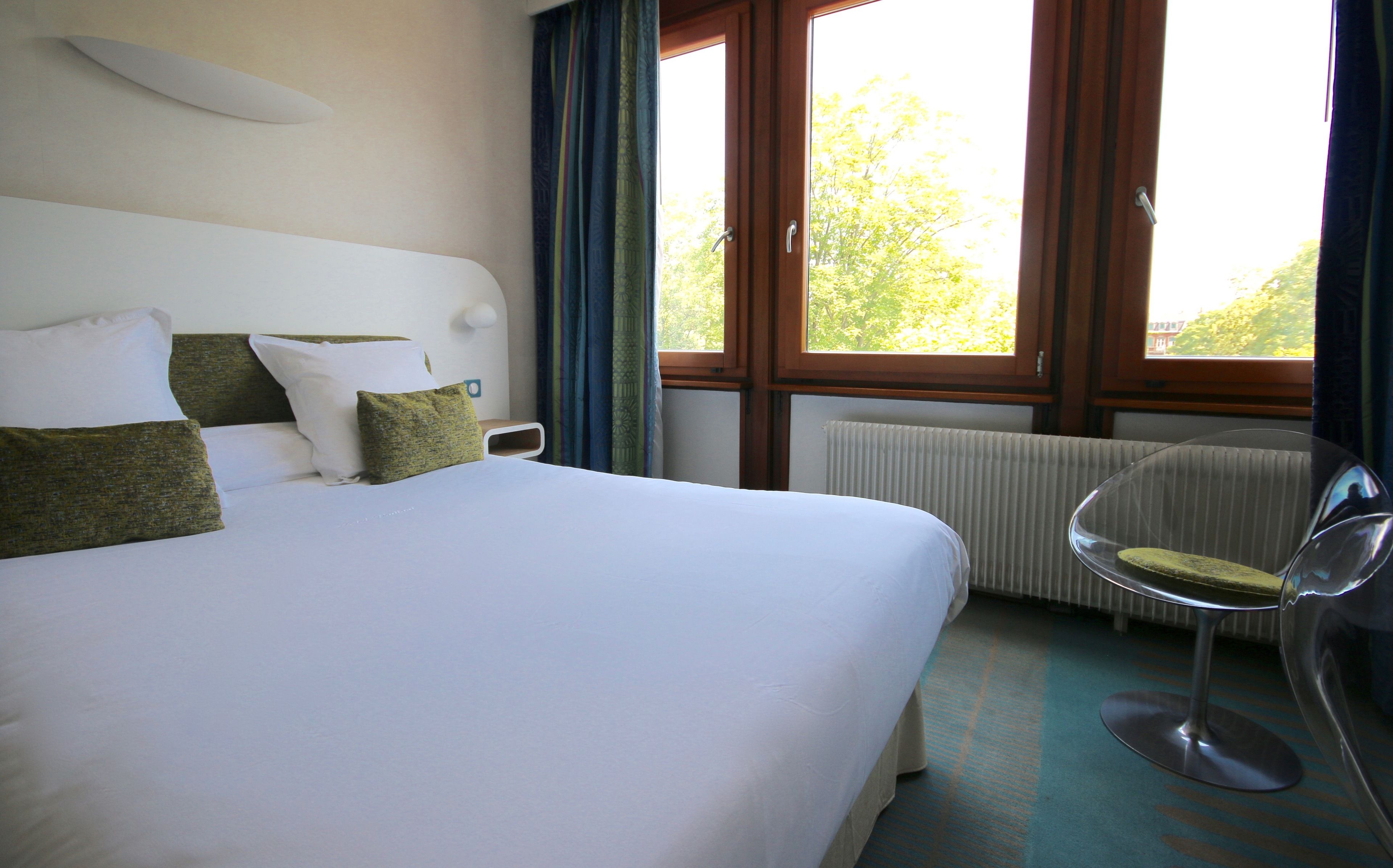 Ein Hotelzimmer mit einem großen Bett, einem Sessel, einem Fenster mit Vorhängen und einer Heizung.