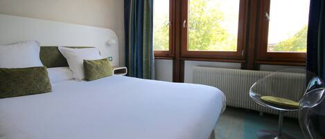 Habitación de hotel con una cama grande, una silla, una ventana con cortinas y un radiador.