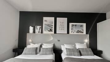 Un dormitorio moderno con dos camas, una pared de acento oscura y obras de arte enmarcadas.