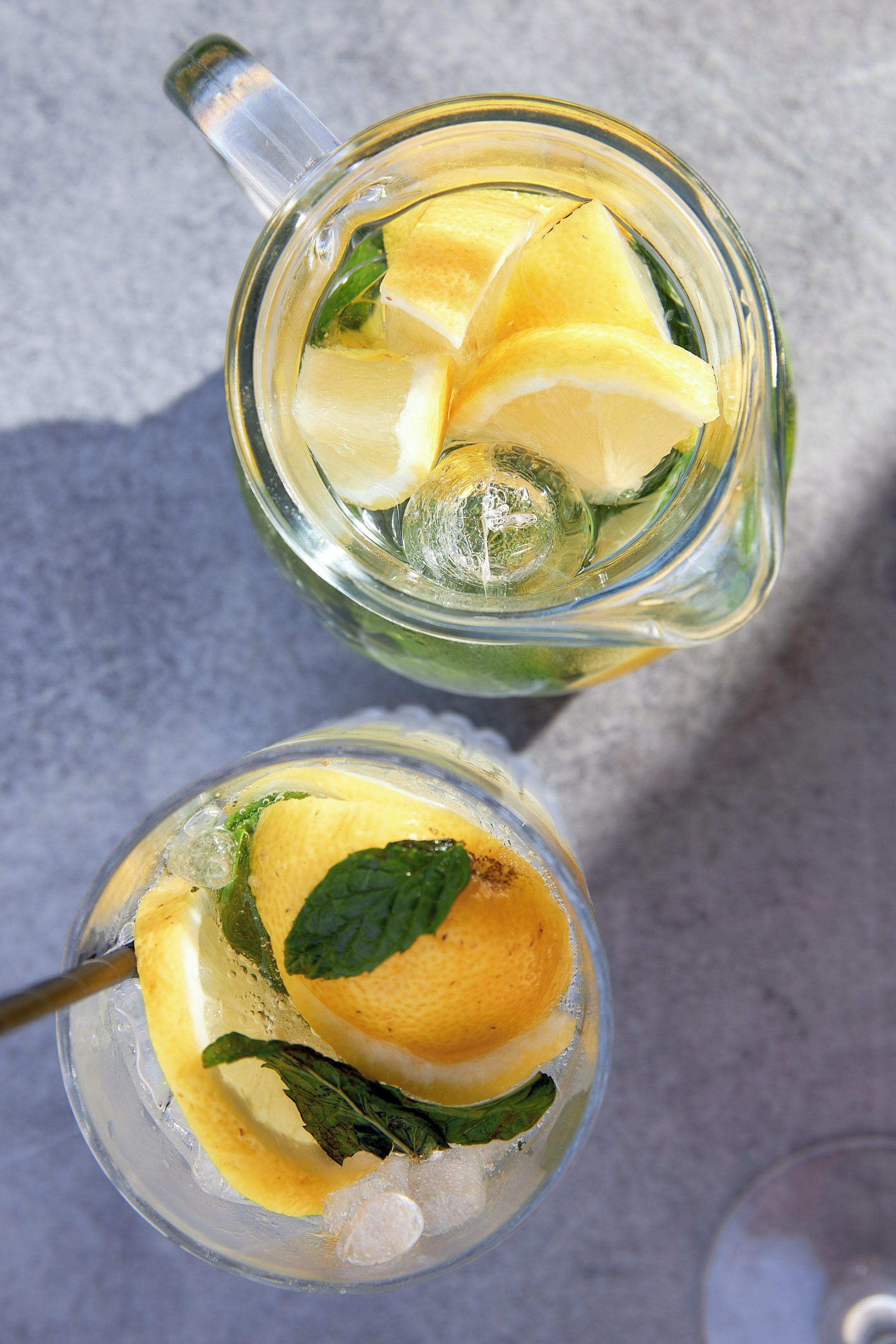 Two glasses of a lemon beverage with mint leaves, ice cubes, and a clear liquid.