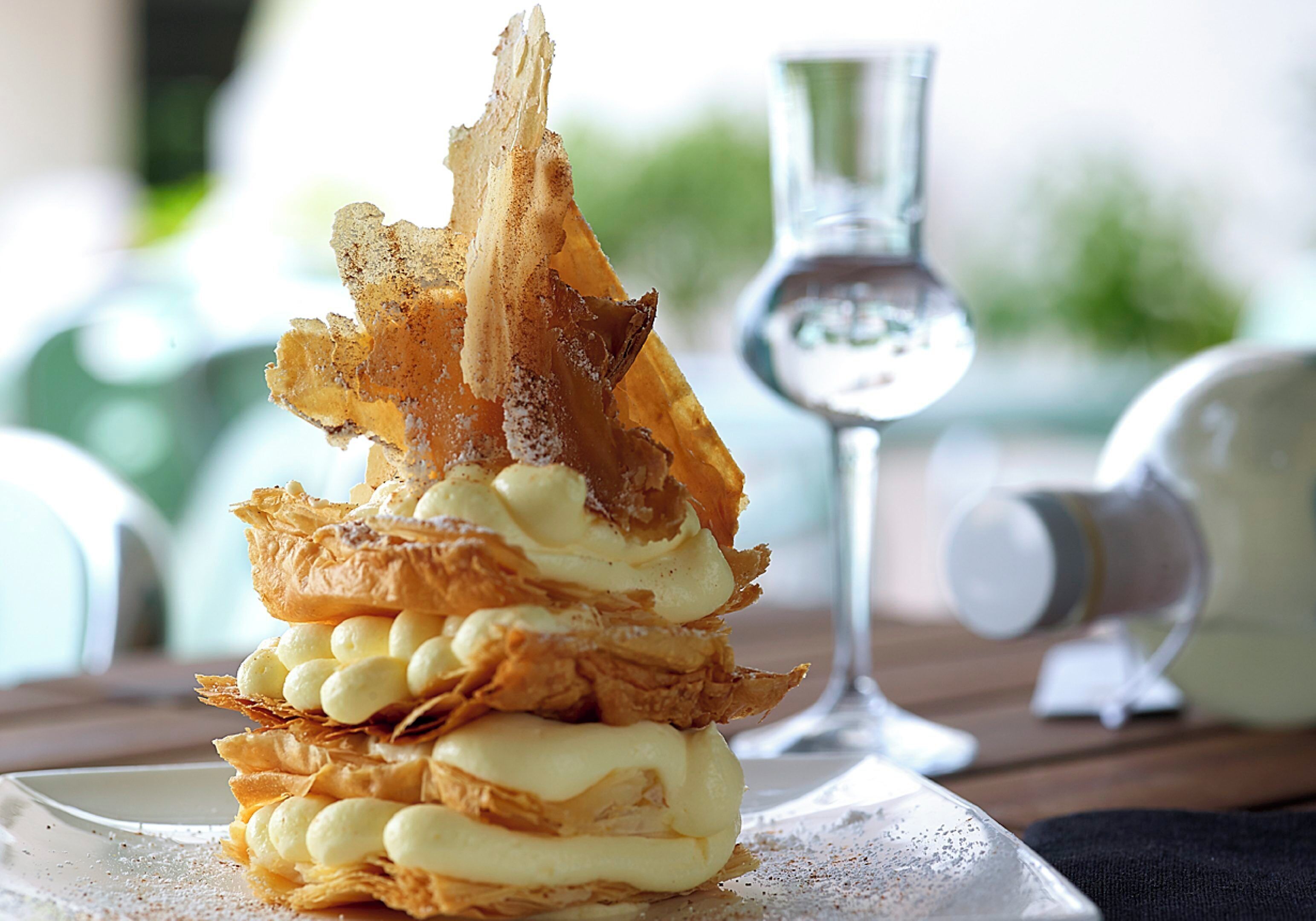 A dessert on a plate with a glass of water and a bottle in the background.