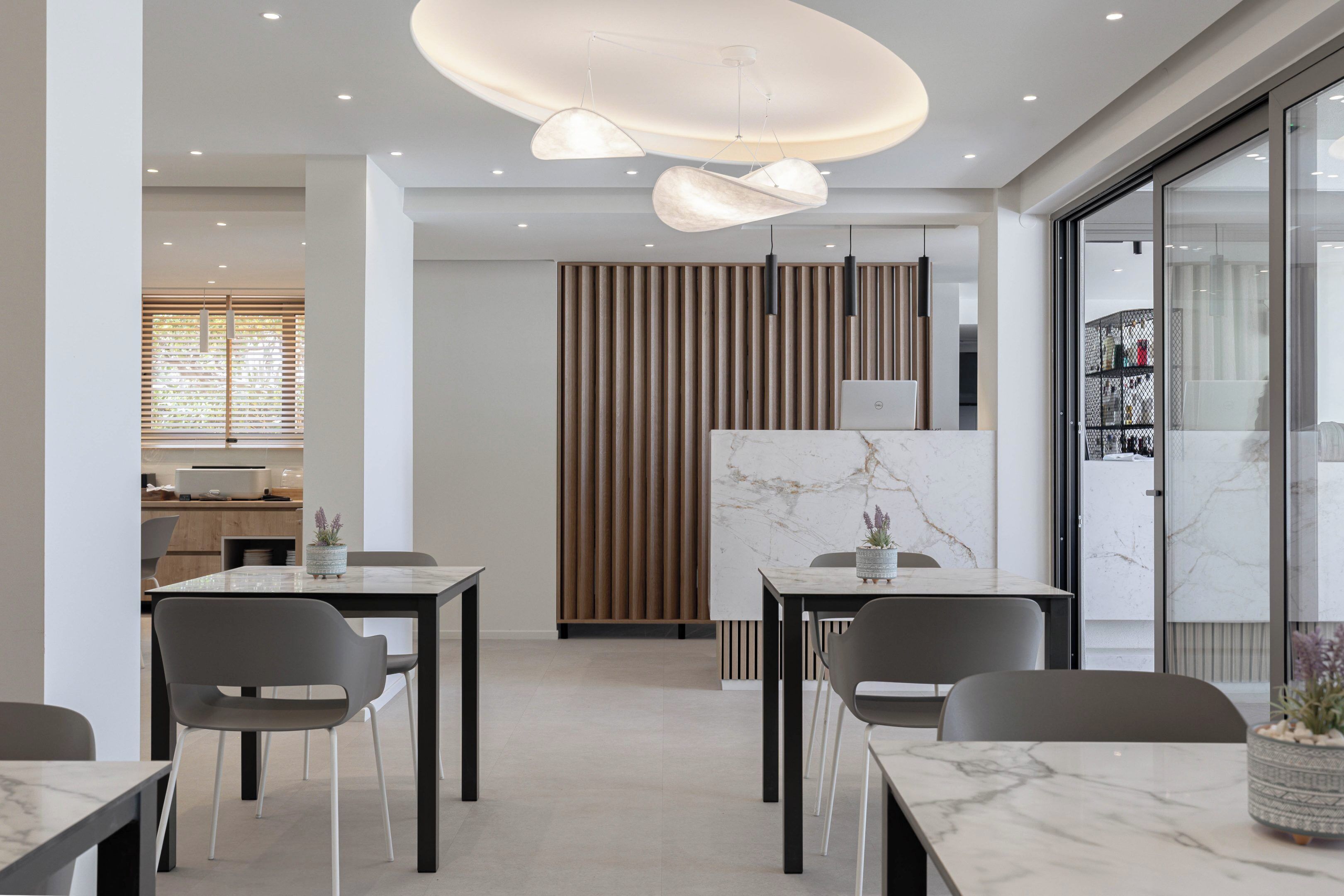 Un'elegante sala da pranzo moderna con tavoli in marmo, sedie grigie, lampade a sospensione e un pannello decorativo in listelli di legno.