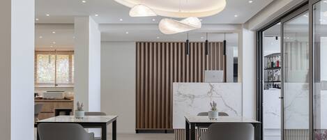 Un'elegante sala da pranzo moderna con tavoli in marmo, sedie grigie, lampade a sospensione e un pannello decorativo in listelli di legno.