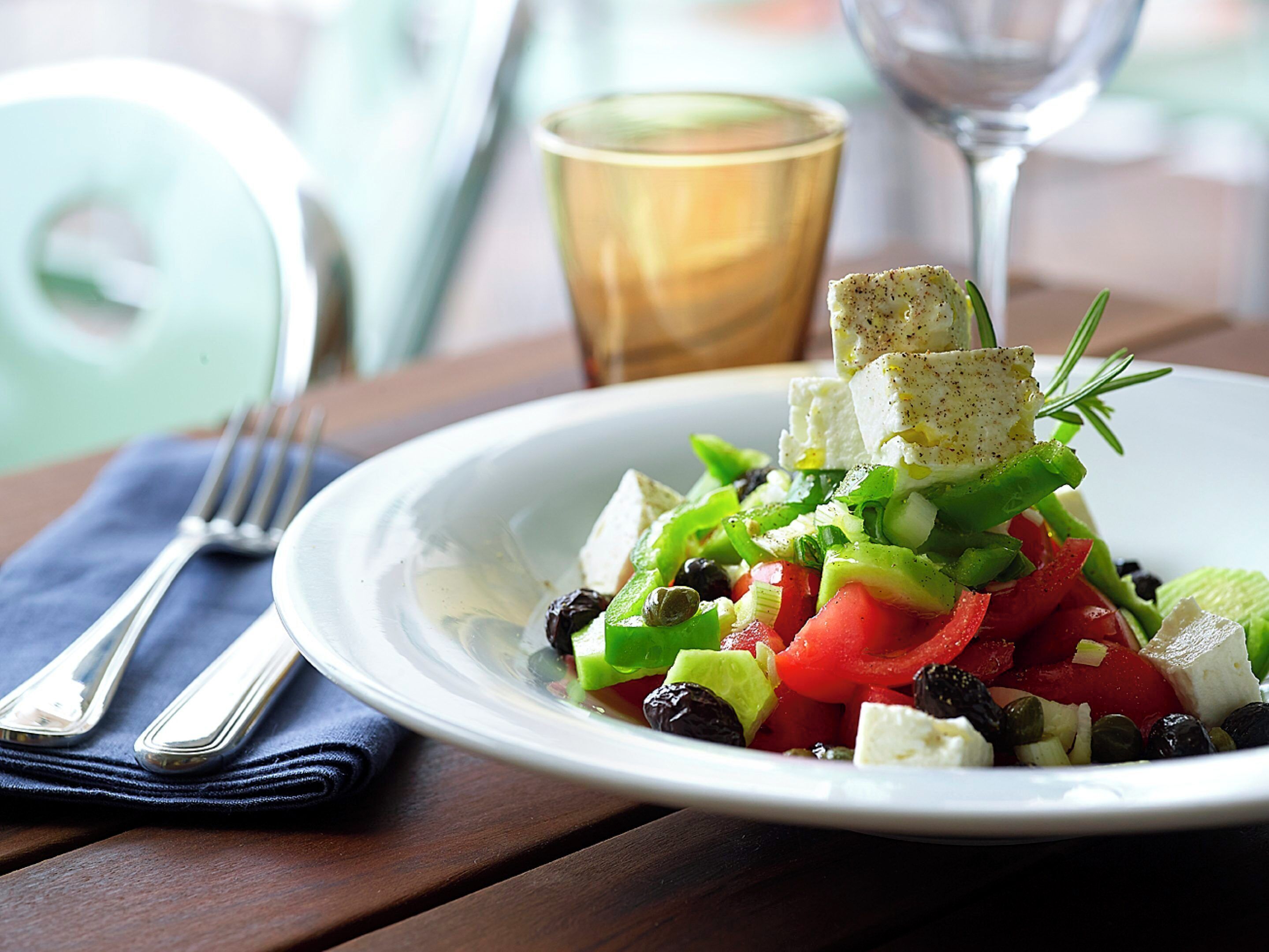 A plate of salad with feta cheese, olives, and vegetables on a wooden table.