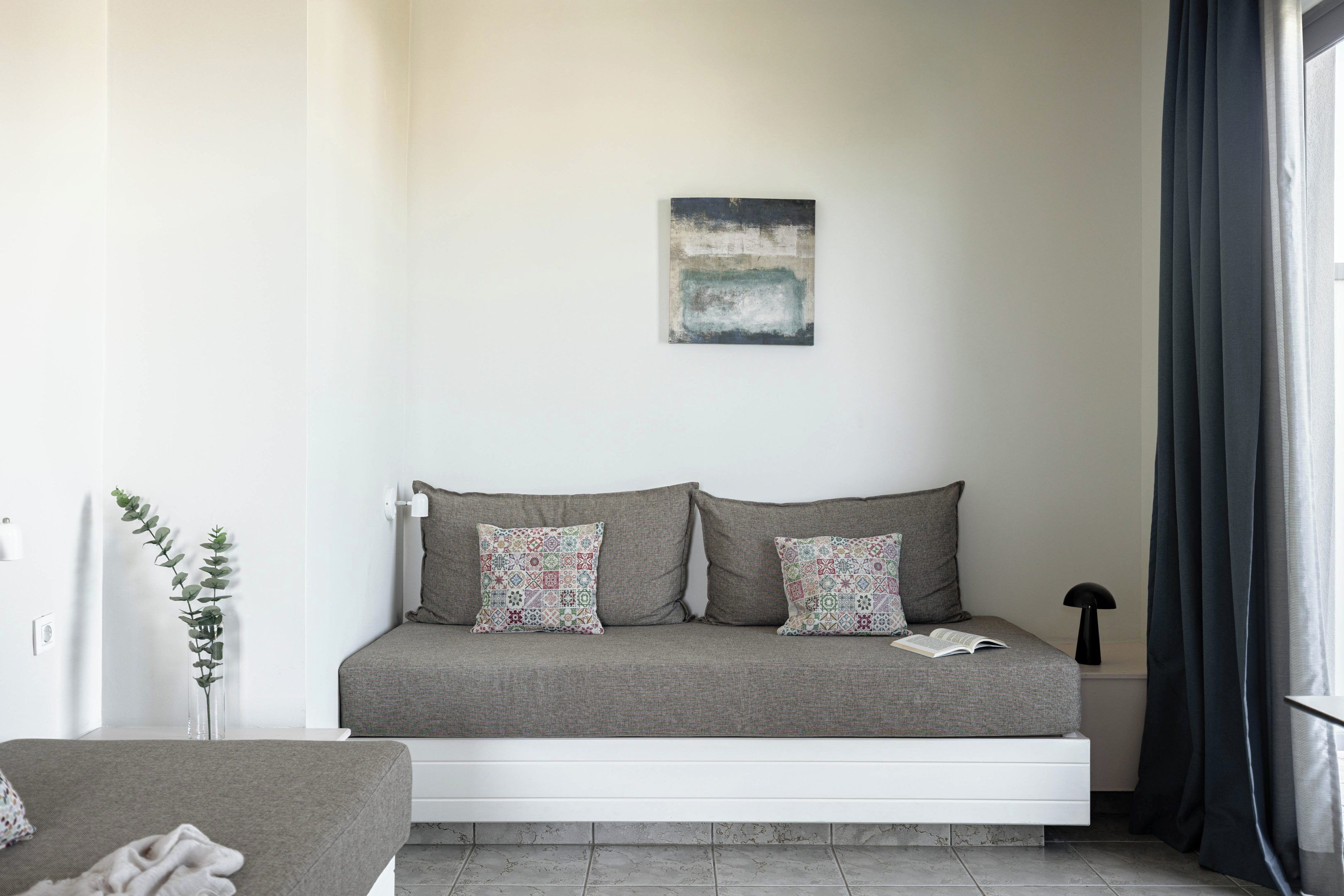 A modern bedroom with a sofa bed, a small bedside table, a lamp, and a wall-mounted abstract painting.