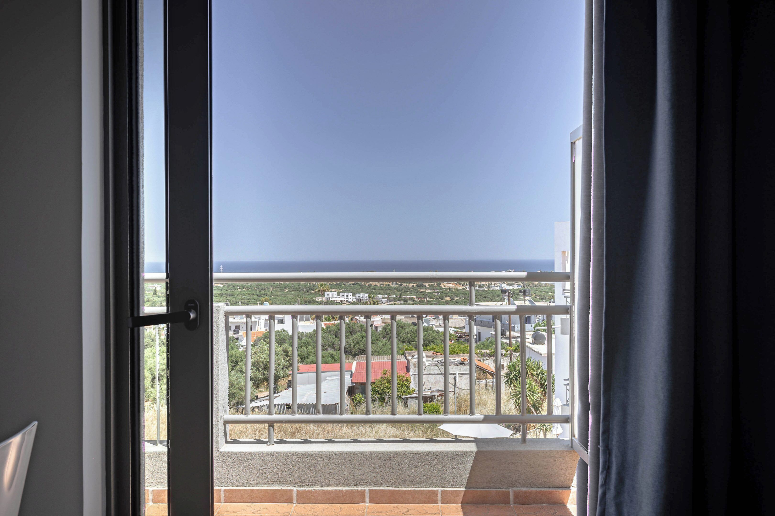 A balcony with a metal railing, a view of buildings, and a clear sky.