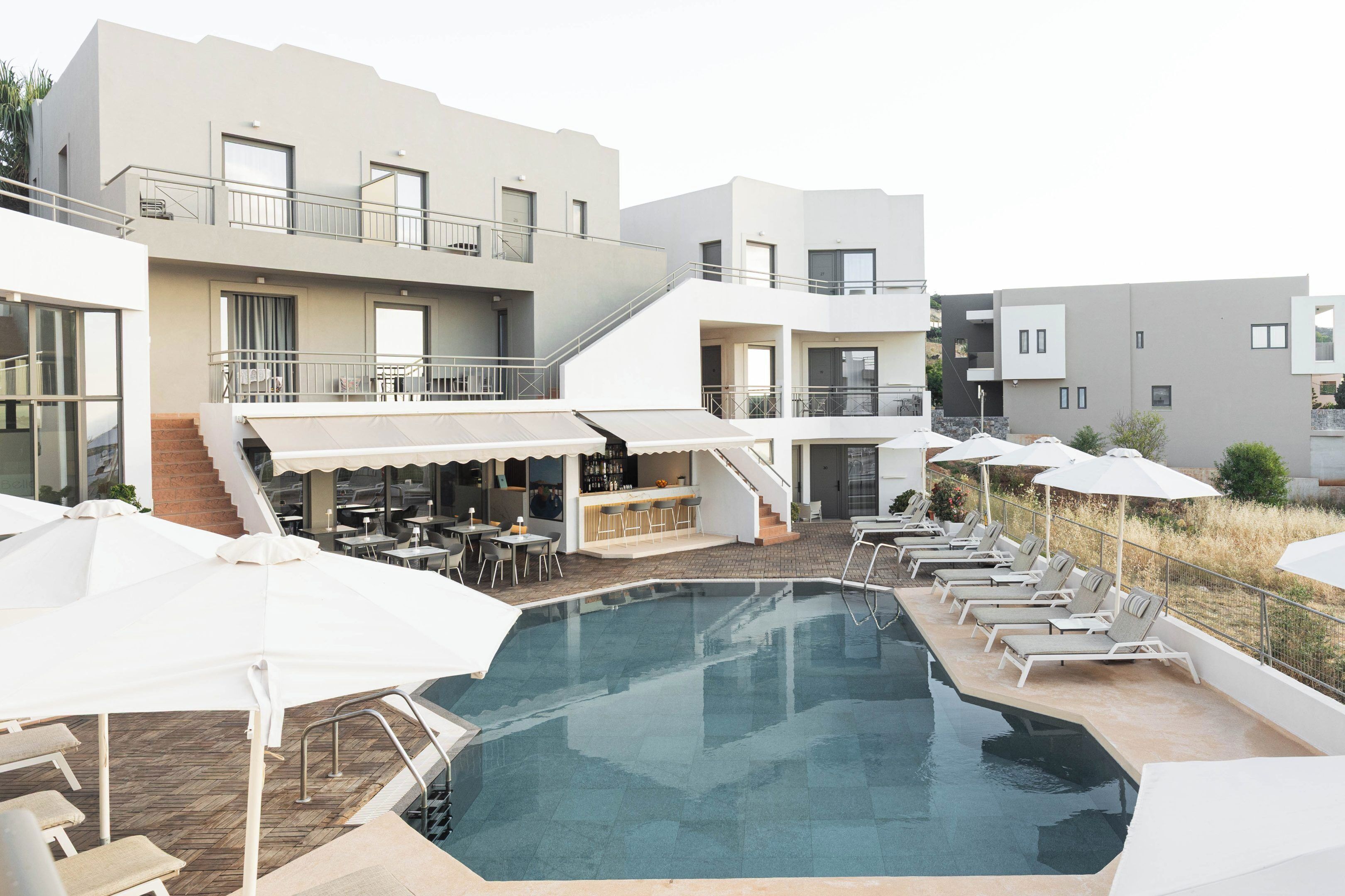 A modern hotel with a swimming pool, outdoor seating, and a bar area.