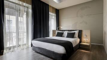 A modern bedroom with a large bed, a nightstand, a lamp, and a view of the outside through sheer curtains.