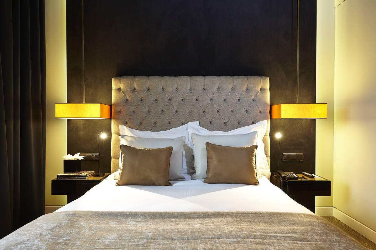 Habitación de hotel con una cama grande, dos lámparas de noche y una mesita de noche con teléfono y libros.