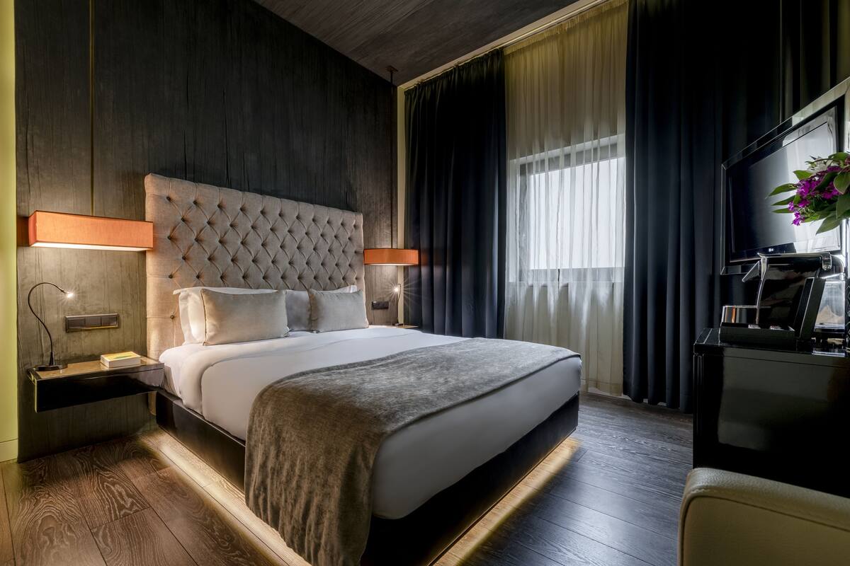 Una habitación de hotel moderna con una cama grande, un televisor y un escritorio con lámpara.