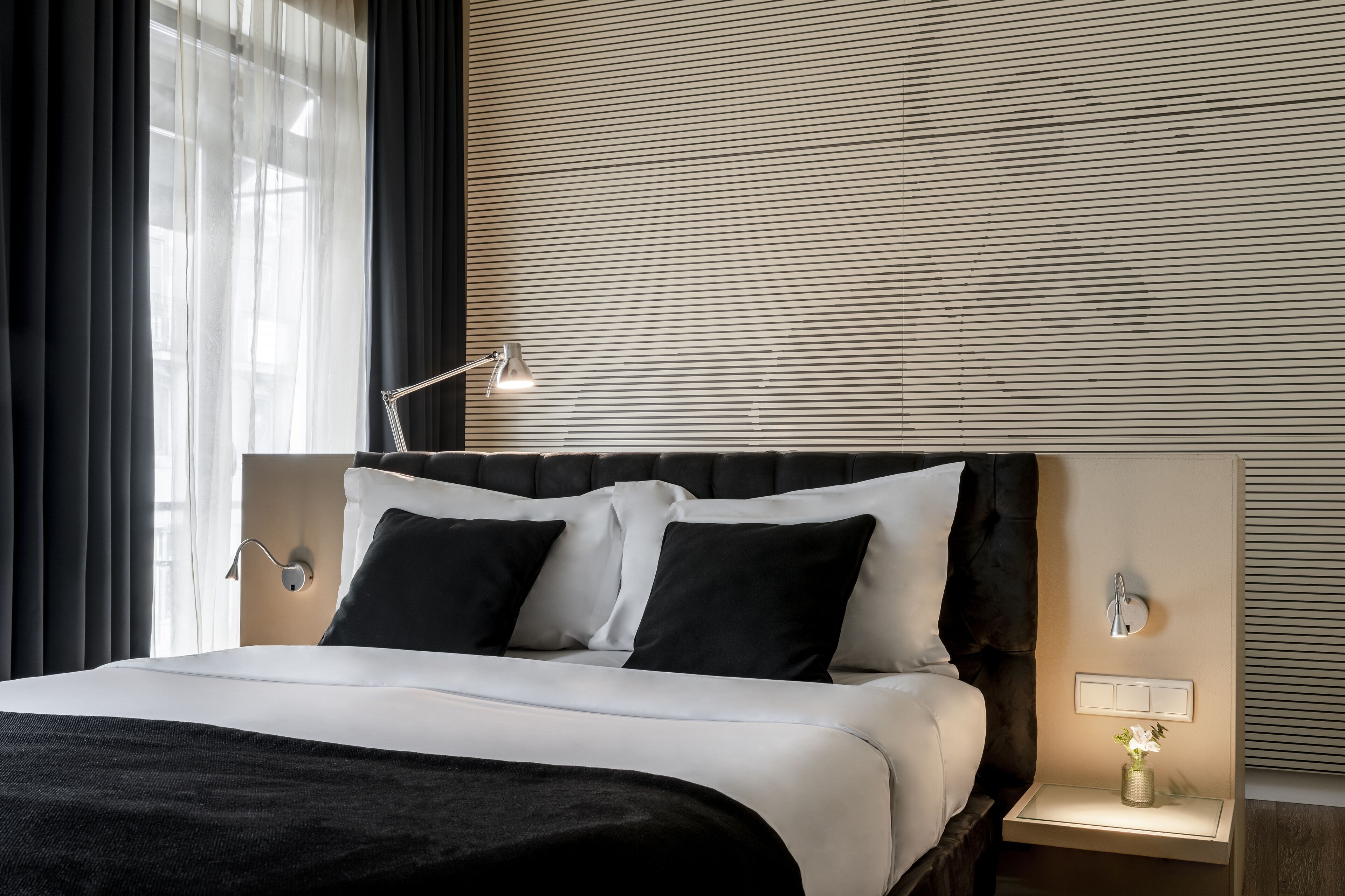 Una habitación de hotel moderna con una cama grande, una mesita de noche con lámpara y un aplique de pared.