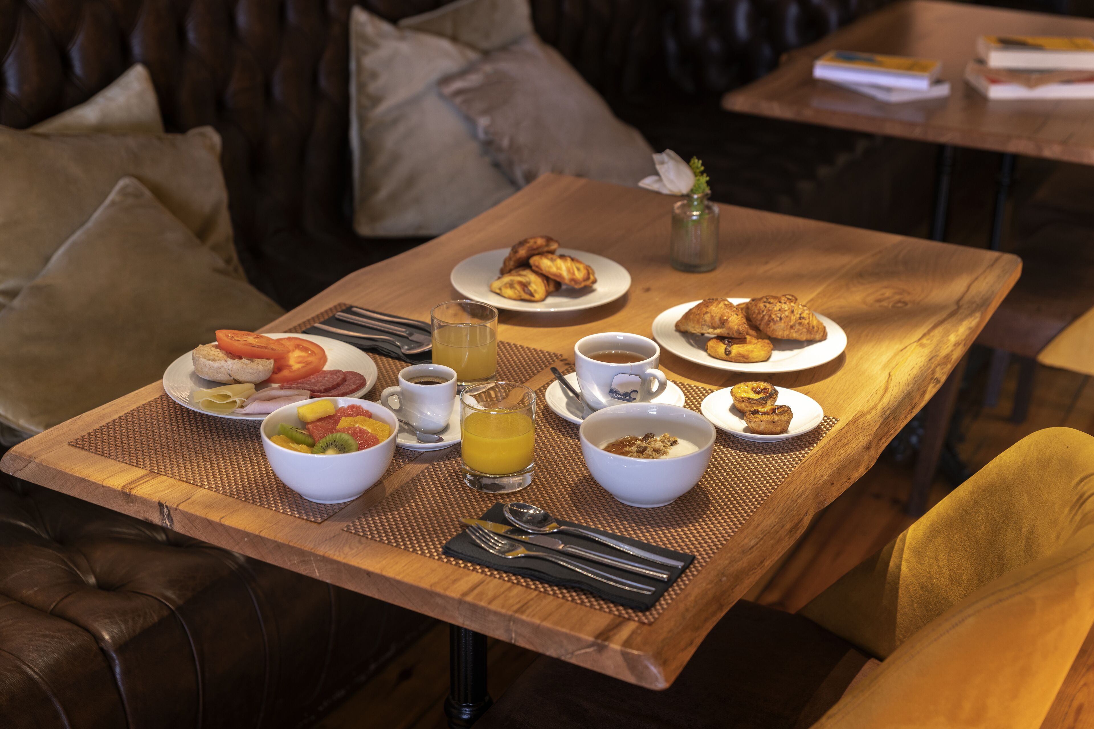 A breakfast table with plates of food, a glass of orange juice, and a bowl of fruit.