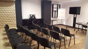 Uma sala de conferências com cadeiras pretas, um quadro branco, uma TV e um bebedouro.