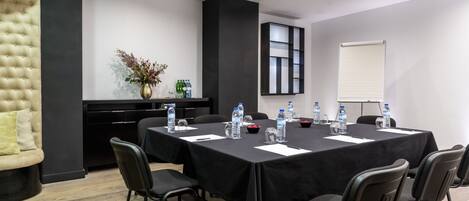 A conference room with a long table, chairs, water bottles, a vase with flowers, and a projector screen.