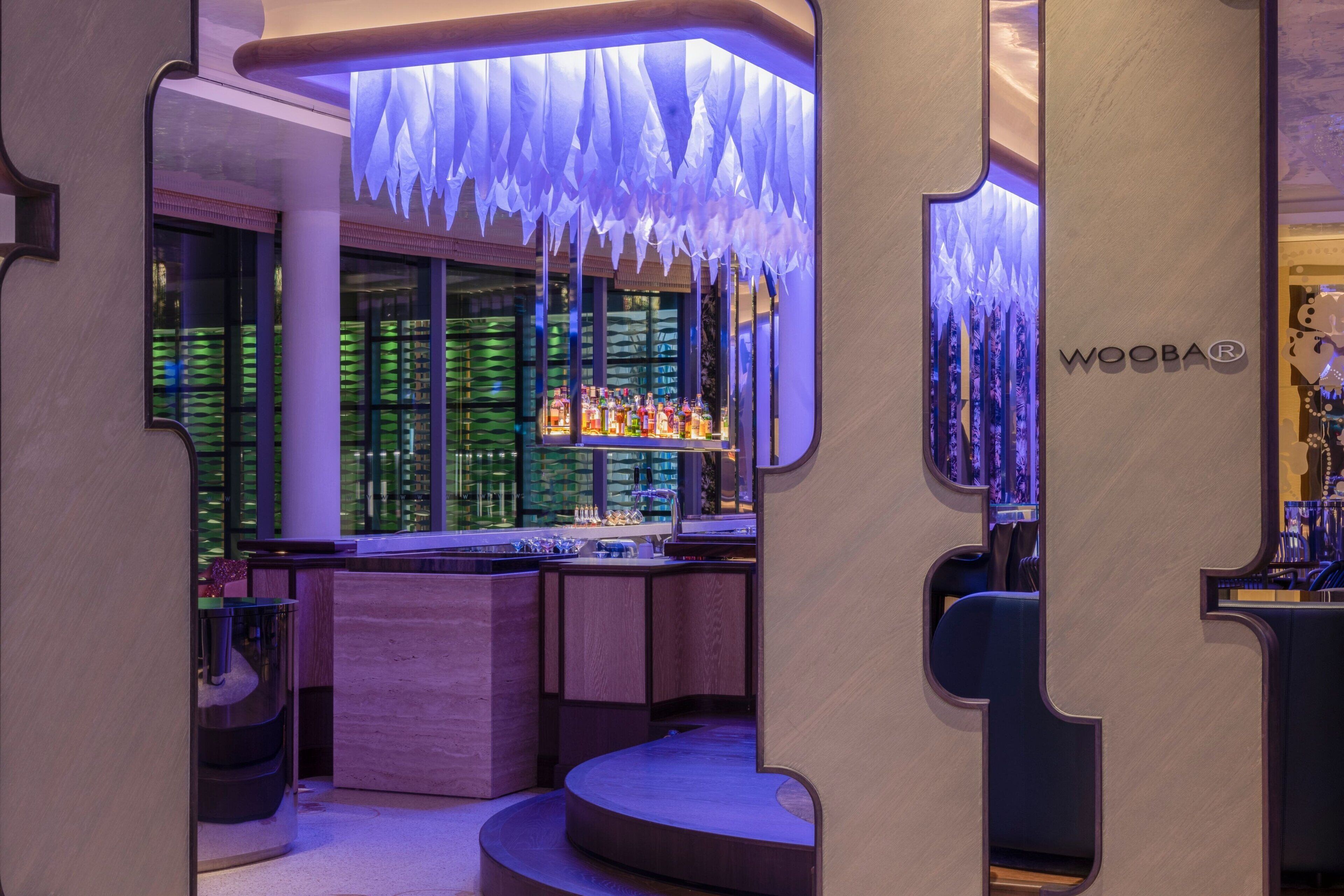 A bar area with a modern design, featuring a counter with various bottles and a sign that reads "WOOBAR".