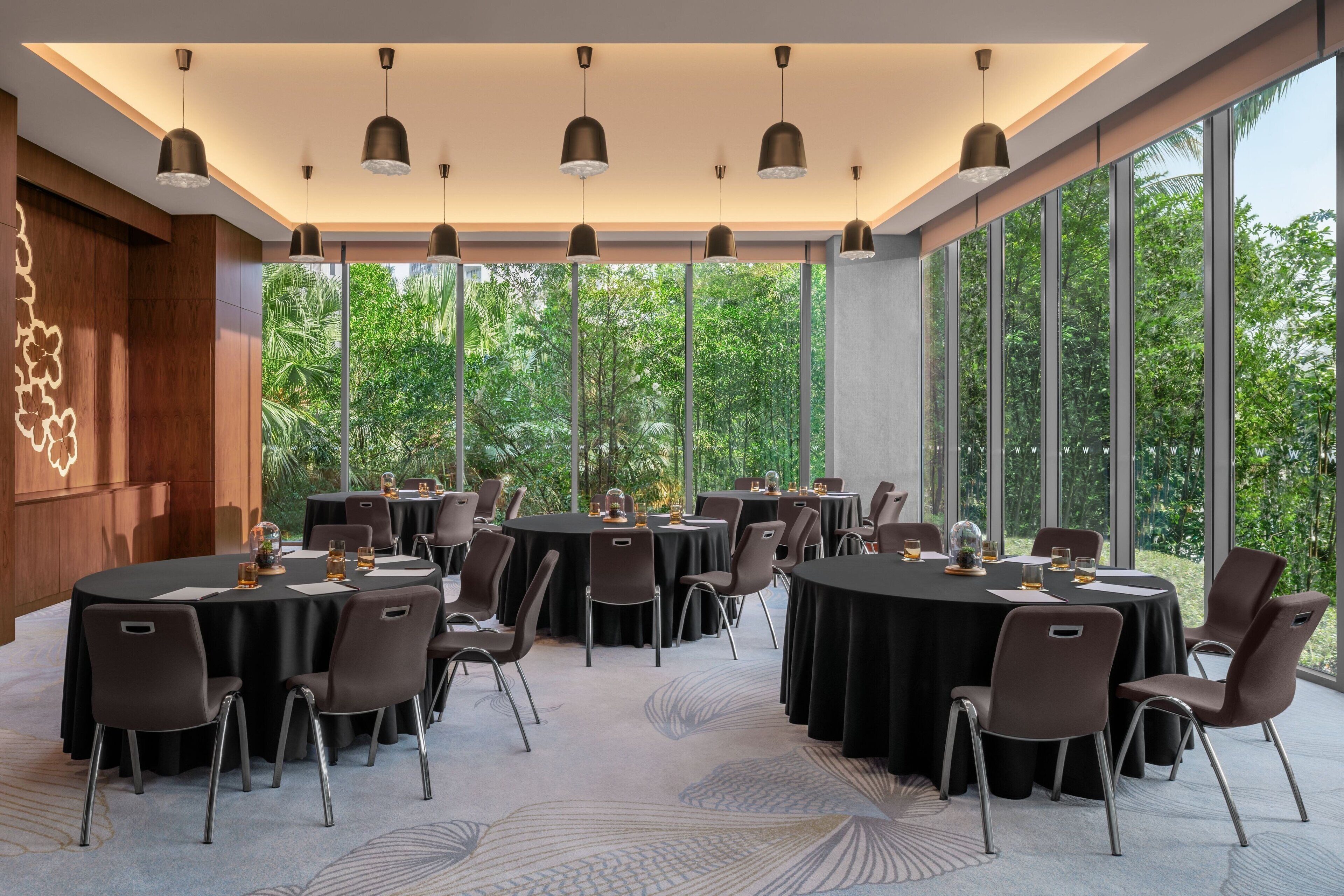 Een congreszaal met ronde tafels, stoelen en hanglampen.