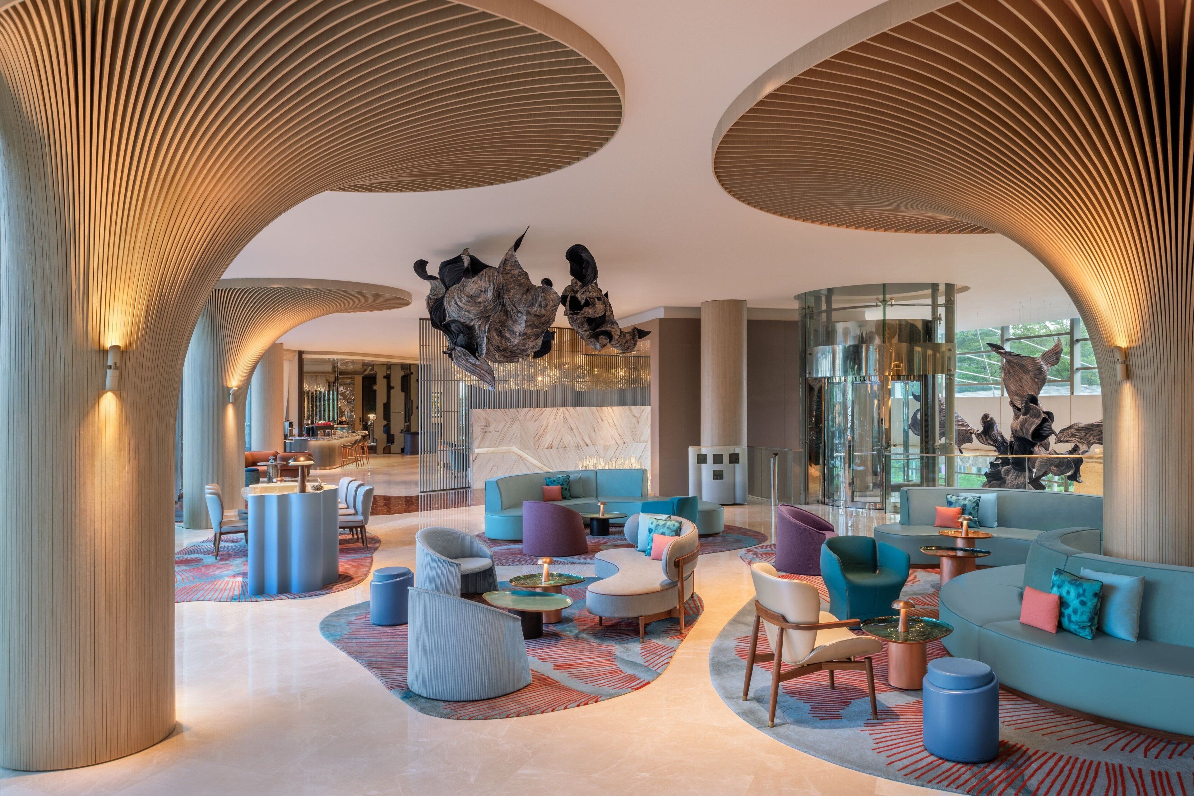 A modern lobby with a central seating area, large pillars, and a glass wall with artwork.