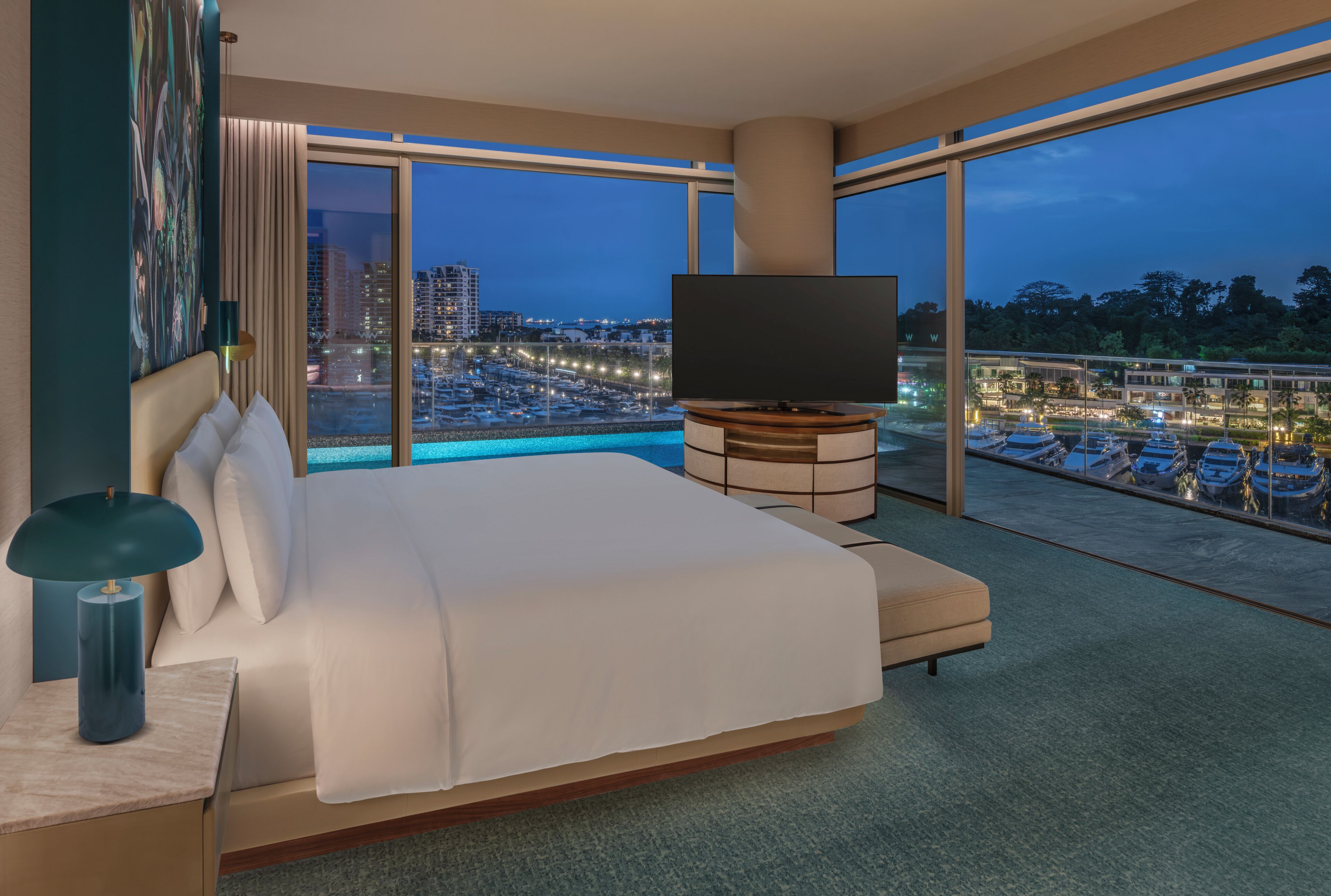 A modern hotel room with a large bed, a flat-screen TV, and a balcony with a city view.