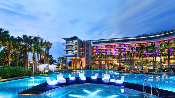 A hotel with a large pool, palm trees, and a modern building with balconies. - W Singapore - Sentosa Cove (Newly Renovated) (Singapore)