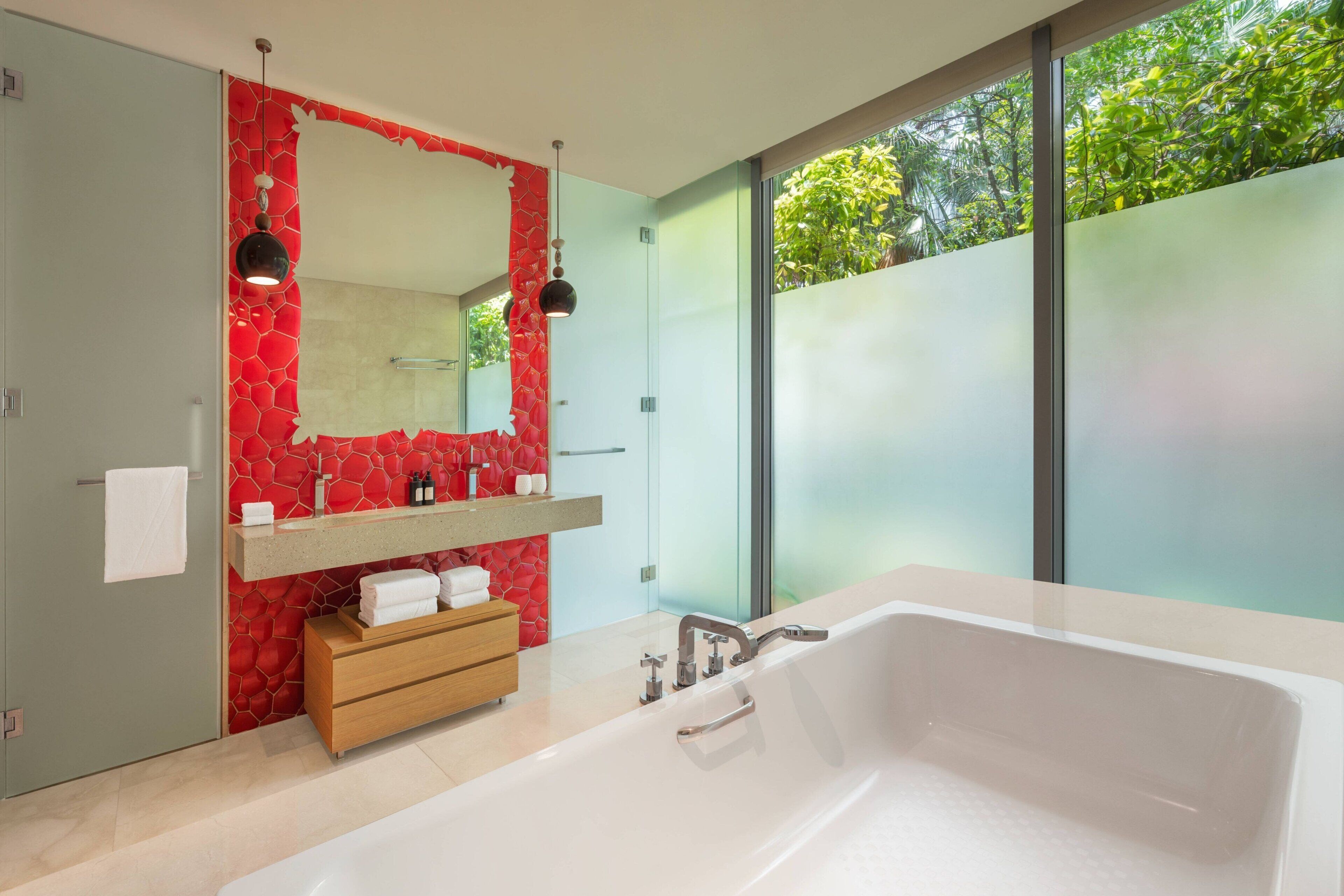 A modern bathroom with a large bathtub, a vanity with a red mosaic backsplash, and a large mirror.