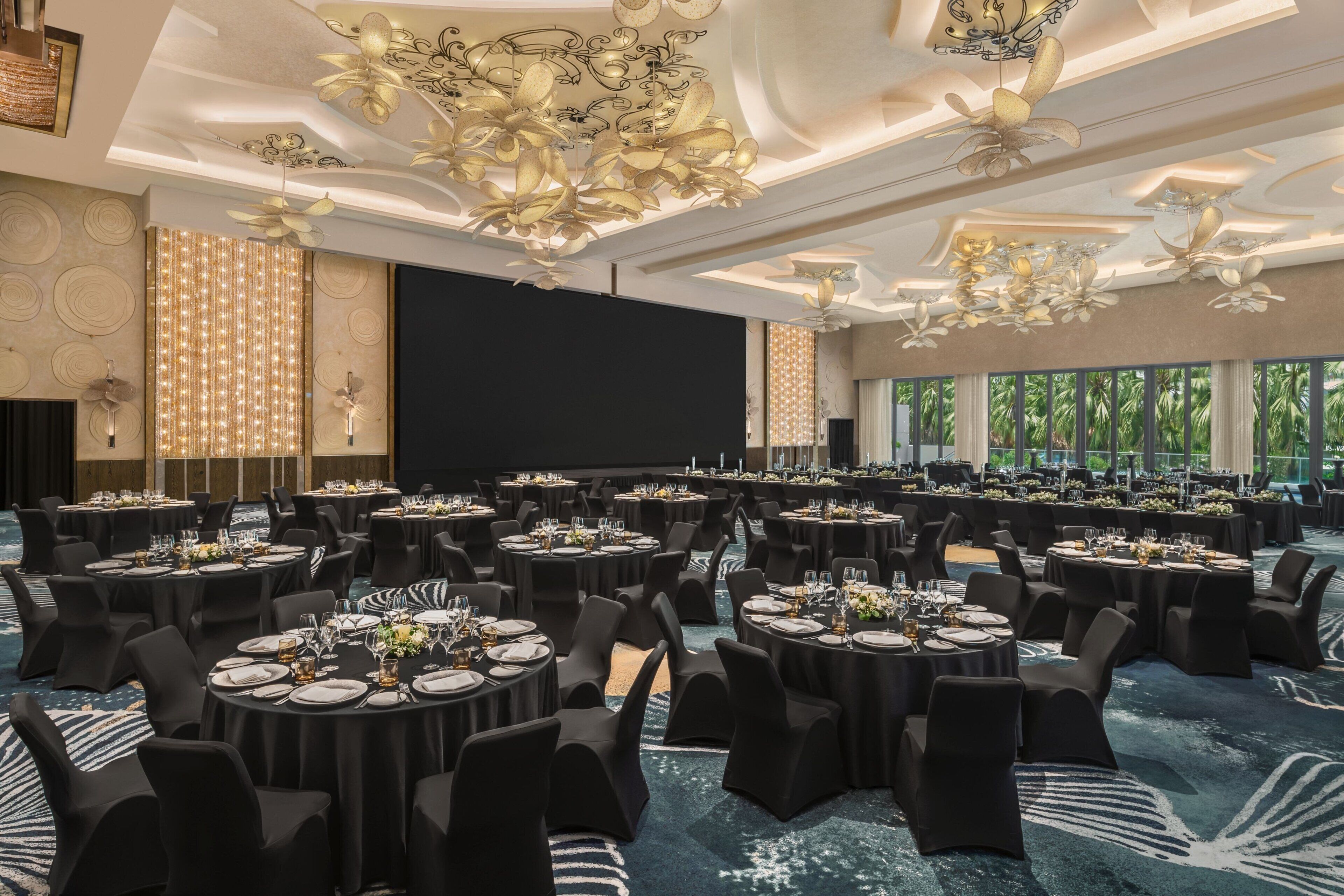 Un salón de banquetes con mesas redondas, sillas negras y una pantalla grande.