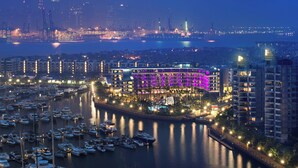 A marina with numerous boats docked, a prominent hotel with purple lighting, and a city skyline in the background. - W Singapore - Sentosa Cove (Newly Renovated) (Singapore)
