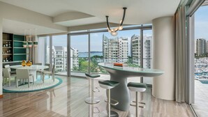 A modern hotel room with a large window, a round dining table, bar stools, and a view of high-rise buildings. - W Singapore - Sentosa Cove (Newly Renovated) (Singapore)