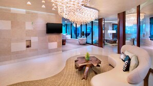 A modern living room with a curved sofa, a wooden coffee table, and a unique ceiling light fixture. - W Singapore - Sentosa Cove (Newly Renovated) (Singapore)