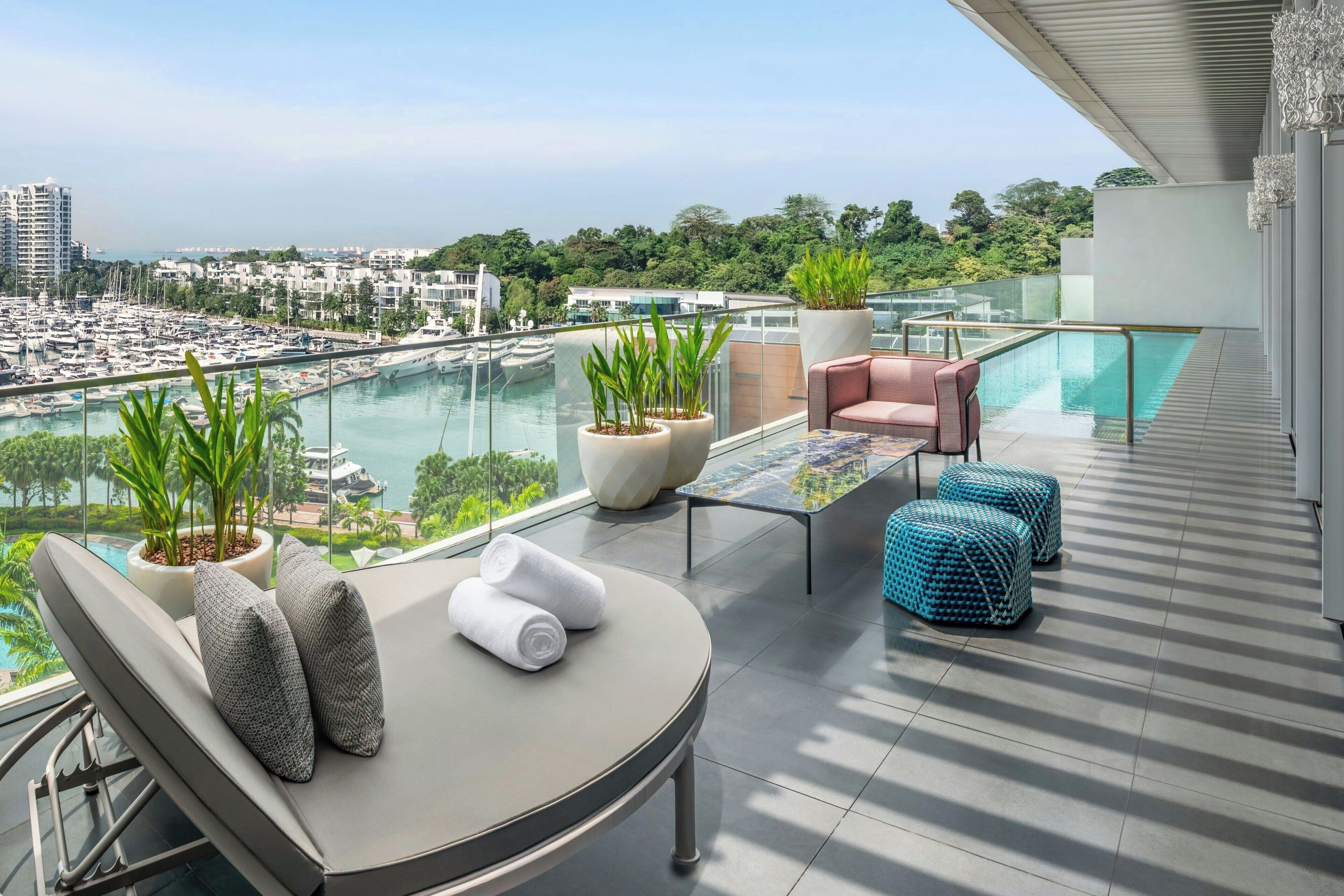 A balcony with a lounge chair, a small table, potted plants, and a view of a marina and cityscape.