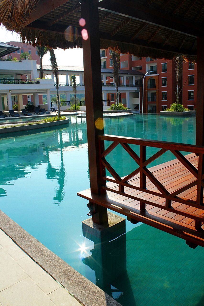A swimming pool with a wooden deck and a thatched roof structure.