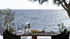 A table set for breakfast with a view of the sea, including plates, cups, and a vase of flowers. - Bellonias Villas (Santorini)