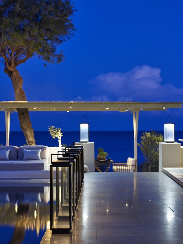 A modern outdoor seating area with a pool, lounge chairs, and a pergola overlooking the ocean.