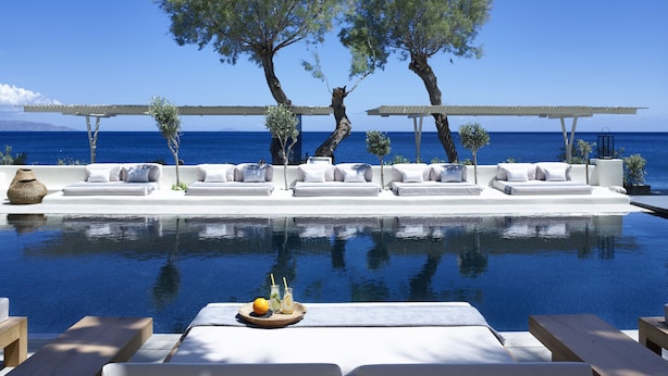 An infinity pool with white lounge chairs and a tray of fruit and drinks. - Bellonias Villas (Santorini)