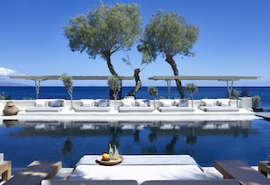 An infinity pool with white lounge chairs and a tray of fruit and drinks.
