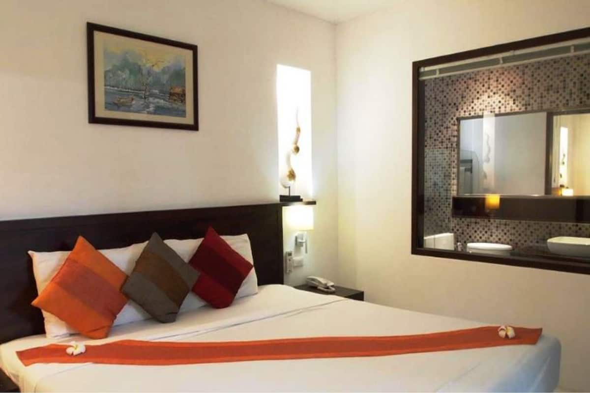Habitación de hotel con cama, mesita de noche, un cuadro en la pared y espejo de baño.