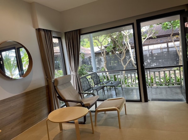 A modern hotel room with a balcony, a round mirror, and a seating area with a table and chairs.