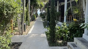 A pathway flanked by tropical plants and palm trees, leading to a covered area with a view of the sea. - Evergreen Resort (Koh Samui)