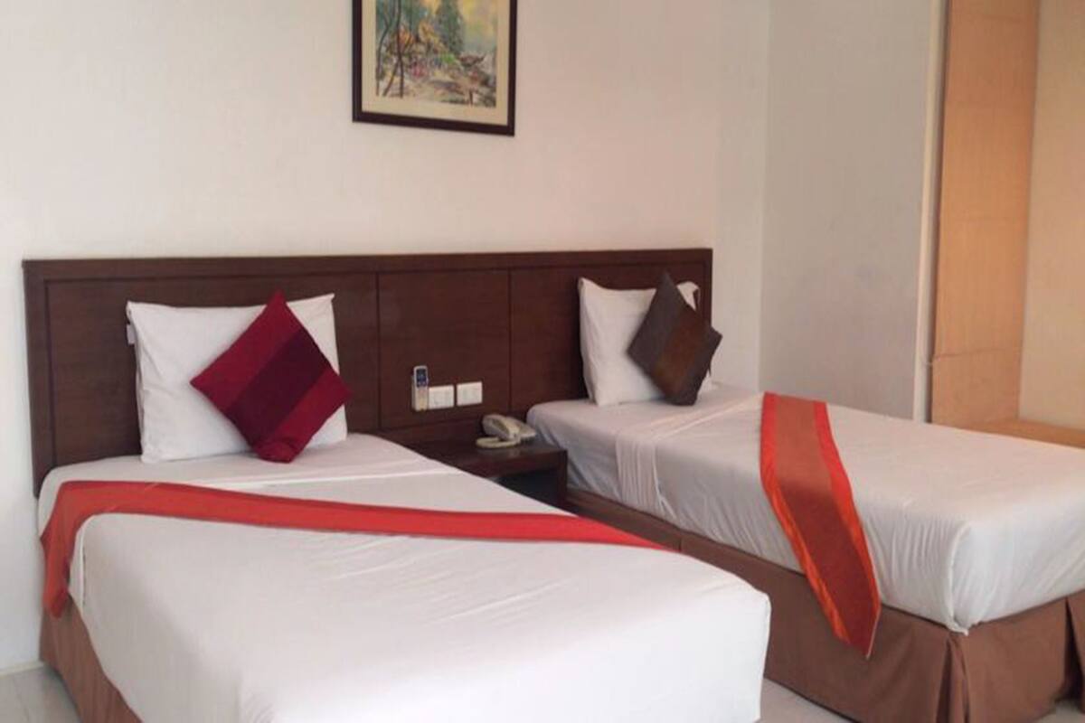 Habitación de hotel con dos camas individuales, cada una con ropa blanca y un detalle en rojo. Hay un cuadro en la pared sobre las camas.