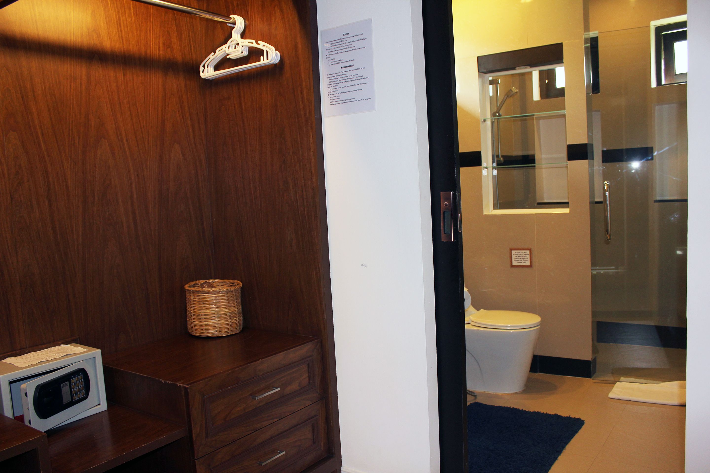 A bathroom with a wooden vanity, a microwave, a wicker basket, a glass shower enclosure, and a white toilet.