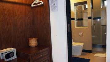 A bathroom with a wooden vanity, a microwave, a wicker basket, a glass shower enclosure, and a white toilet.