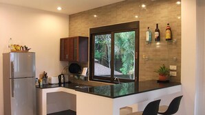 A modern kitchen with a built-in refrigerator, a window with a view of greenery, and a bar area with two stools. - Leelawadee Garden Resort (Krabi)