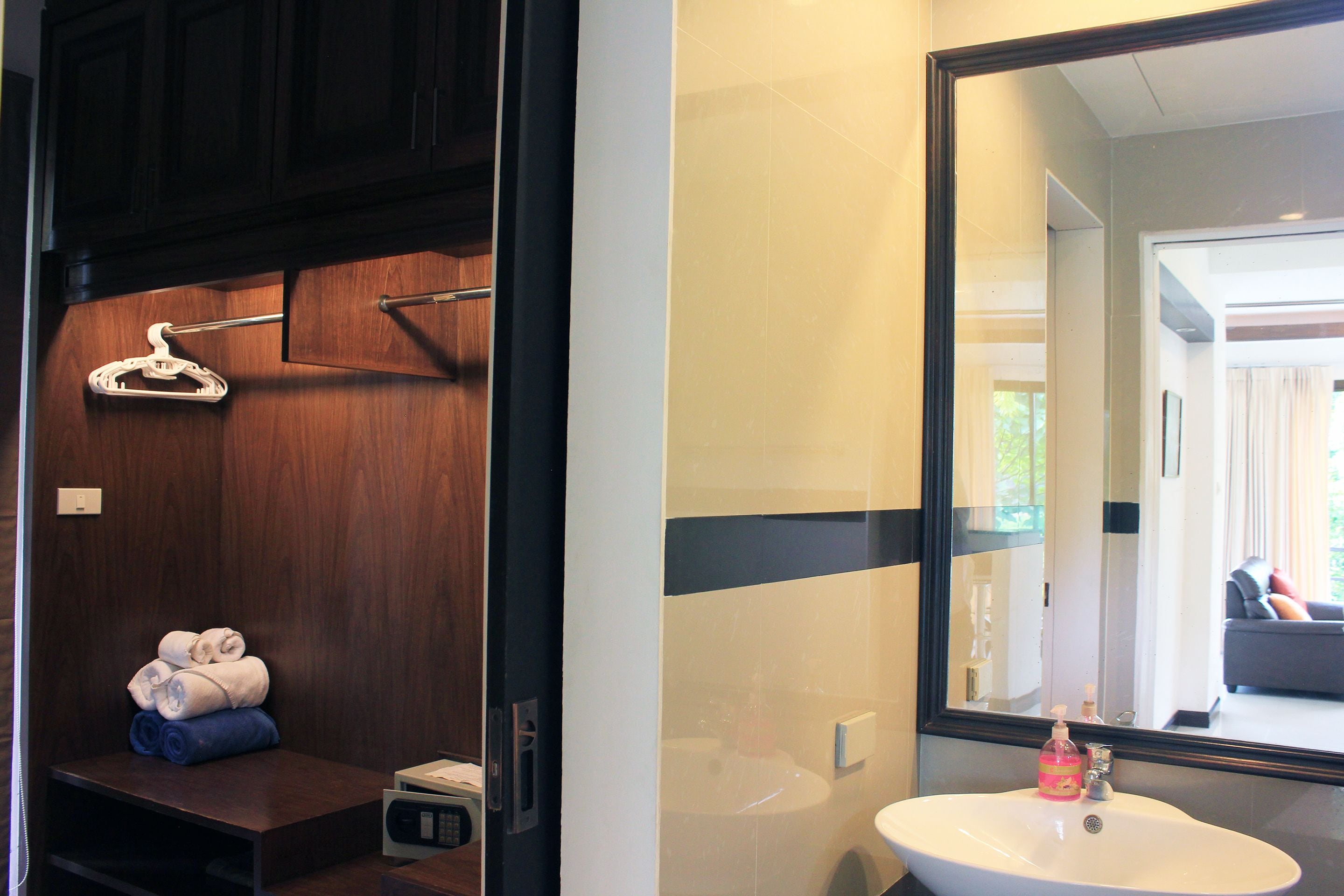 Une salle de bain avec un meuble-lavabo en bois, un lavabo blanc et un miroir qui reflète le salon.